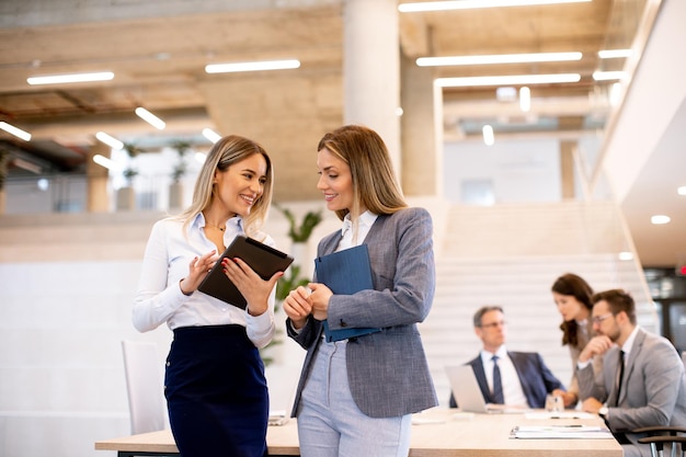 Deux jeunes femmes d'affaires regardant les résultats financiers sur une tablette numérique devant leur équipe au bureau