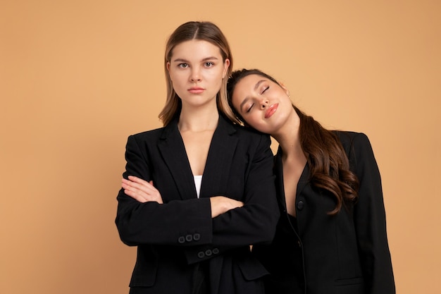 Deux jeunes femmes d'affaires vêtues d'un costume noir debout studio fond de couleur orange