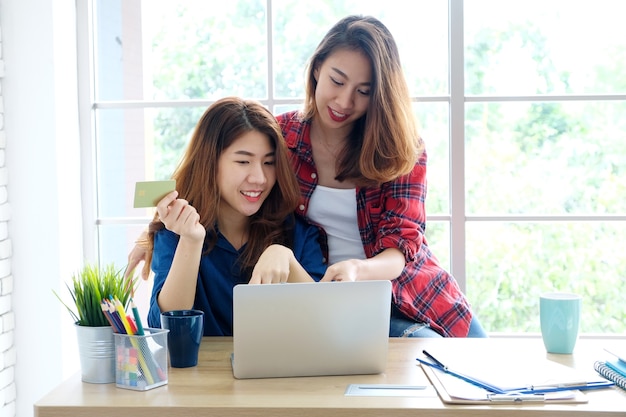 Deux jeunes femmes asiatiques détenant une carte de crédit et utilisant un ordinateur portable pour faire leurs achats en ligne