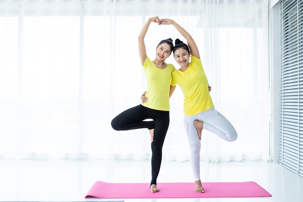 Deux jeunes femmes asiatiques s'entraînent à pratiquer le yoga en robe jaune ou posent avec un entraîneur et pratiquent la méditation, le mode de vie bien-être et le concept de remise en forme dans une salle de sport.