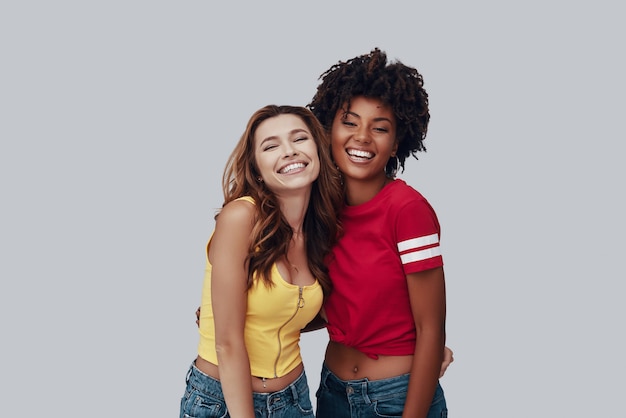 Deux jeunes femmes attirantes regardant la caméra et souriant en se tenant debout sur fond gris