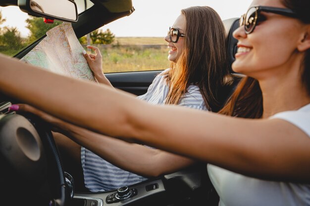 Deux jeunes femmes brunes à lunettes de soleil sont assises dans un cabriolet noir par une journée ensoleillée. L'un d'eux garde la carte dans ses mains. .