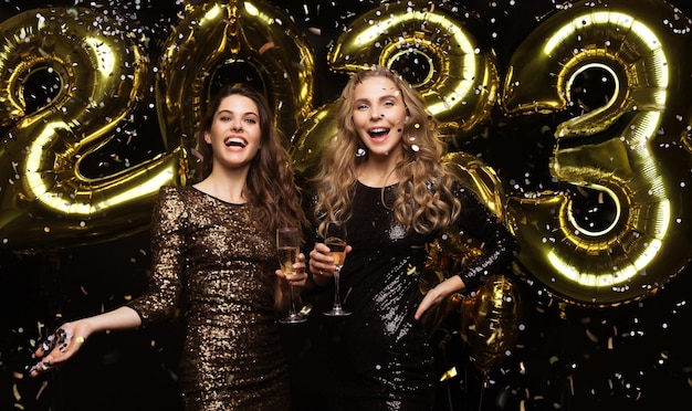 Deux jeunes femmes buvant du champagne Image de filles avec des ballons isolés sur fond noir s'amusant à la fête du Nouvel An 2023