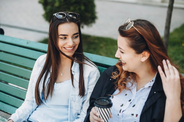 Deux jeunes femmes caucasiennes parlant souriant alors qu'il était assis sur un banc à l'extérieur de boire du café.