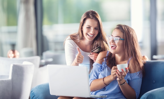 Deux jeunes femmes dans un café avec une carte de crédit et un ordinateur portable les achètent confortablement sur Internet