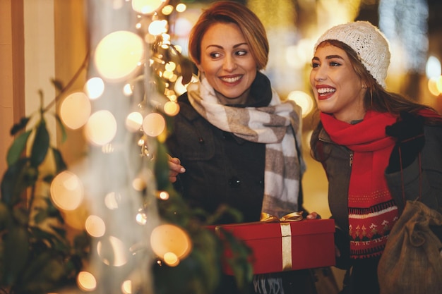 Deux jeunes femmes gaies s'amusent dans la rue de la ville la nuit de Noël. Ils rient et achètent des cadeaux pour les vacances à venir.