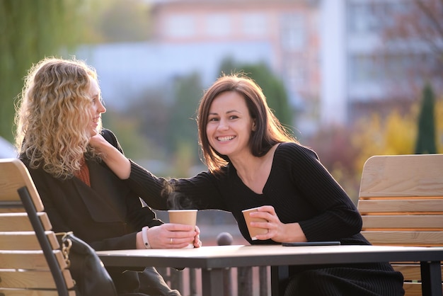 Deux jeunes femmes heureuses assises au café de la rue de la ville s'amusant ensemble pendant la pause-café