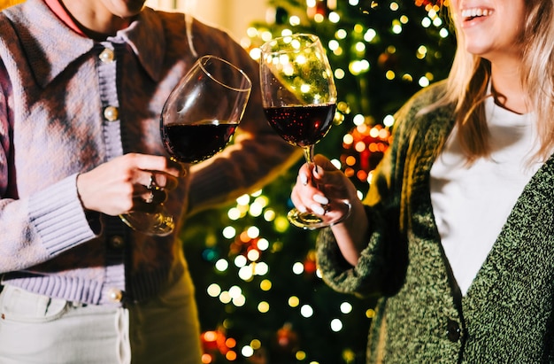 Photo deux jeunes femmes heureuses grillant et buvant du vin près de l'arbre de noël.