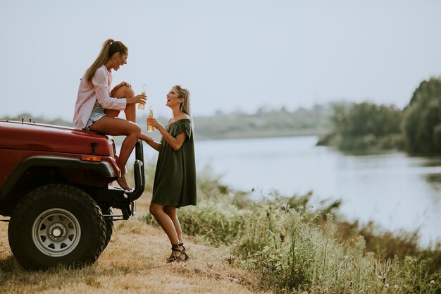 Deux jeunes femmes heureux de boire du cidre par le véhicule au bord du lac