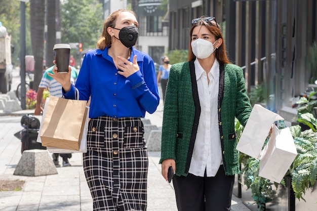 Deux jeunes femmes marchent dans la rue portant des masques faciaux parlant joyeusement après le shopping