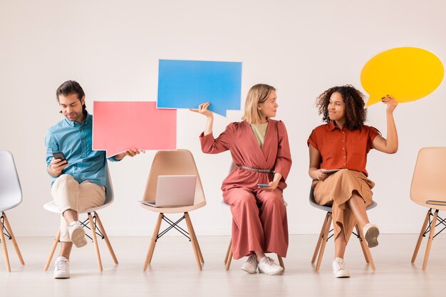 Deux jeunes femmes millénaires interculturelles avec des gadgets mobiles et des bulles de papier communiquant en publiant sur les réseaux sociaux