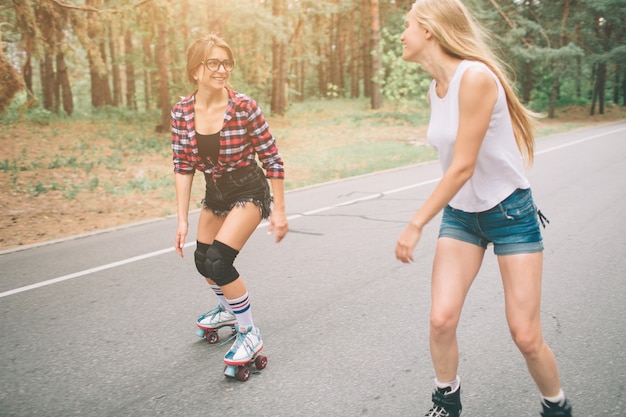 Photo deux jeunes femmes minces et sexy et patins à roulettes. une femelle a des patins à roues alignées et l'autre a des patins à quatre roues. les filles montent dans les rayons du soleil