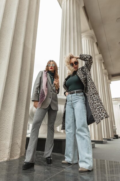 Deux jeunes femmes de mode avec des vêtements vintage d'automne à la mode se tiennent près d'une colonne de bâtiment dans la rue