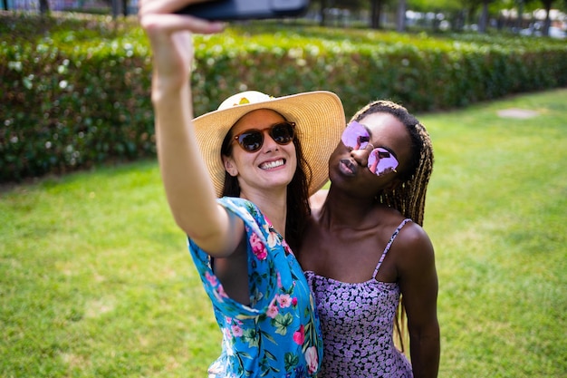 Deux jeunes femmes multiethniques avec des robes d'été prenant un selfie dans un jardin