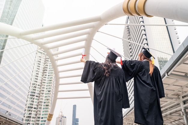 Deux jeunes femmes portant une robe universitaire levant la main avec succès Baccalauréat universitaire