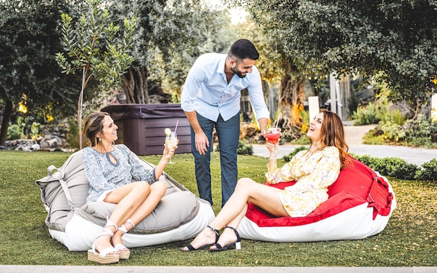 Deux jeunes femmes se font servir des boissons par un ami masculin lors d'un cocktail dans le concept de style de vie de l'heure d'été du jardin