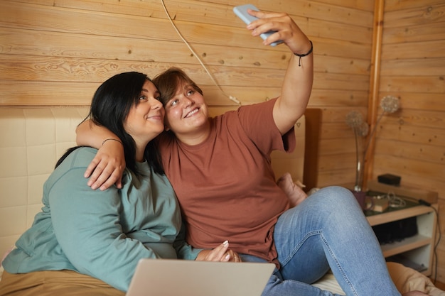 Deux jeunes femmes se reposant sur le lit ensemble et faisant un portrait de selfie sur leur téléphone mobile