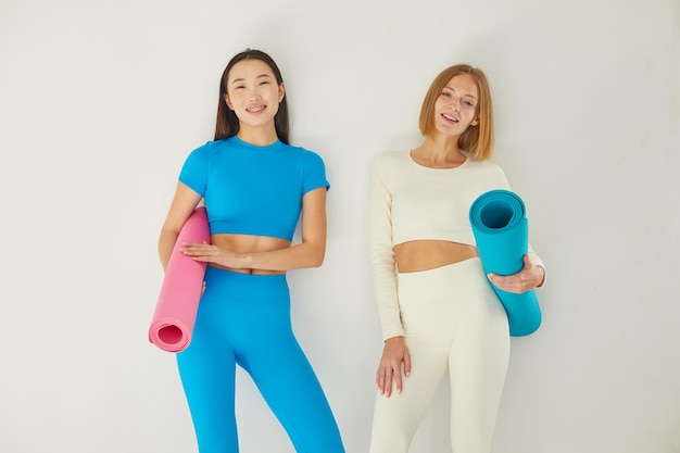 Photo deux jeunes femmes se tiennent dans une classe de yoga et sourient concept de soins de santé physique et mentale ethnie asiatique et caucasienne