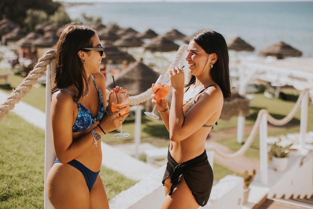 Deux jeunes femmes souriantes en bikini profitant de vacances sur la plage tout en buvant un cocktail