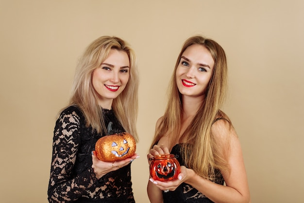 Deux jeunes femmes souriantes tenant des citrouilles d'Halloween sur fond beige