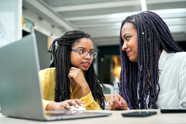 Deux jeunes femmes souriantes travaillant ensemble dans un bureau à l'aide d'un ordinateur portable