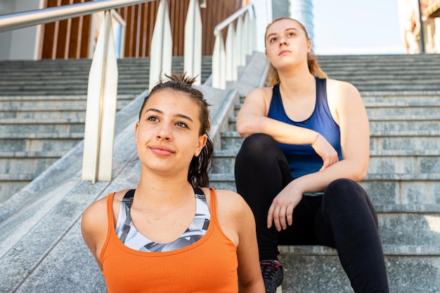 Deux jeunes femmes sportives se reposant après une séance de course sur des gradins, des sportifs intéressés par leur bien-être physique et leur santé