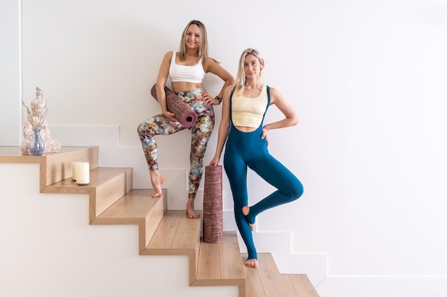 Deux jeunes femmes tenant un tapis de yoga en vêtements de sport dans un entraînement de professeur de yoga en studio blanc