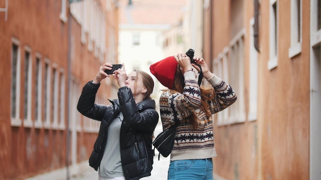 Deux jeunes femmes voyageant dans des vêtements chauds marchant dans les rues étroites en prenant des photos sur l'appareil photo