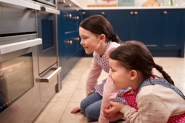 Deux jeunes filles en attente de cupcakes à cuire à la recherche dans le four dans la cuisine à la maison ensemble