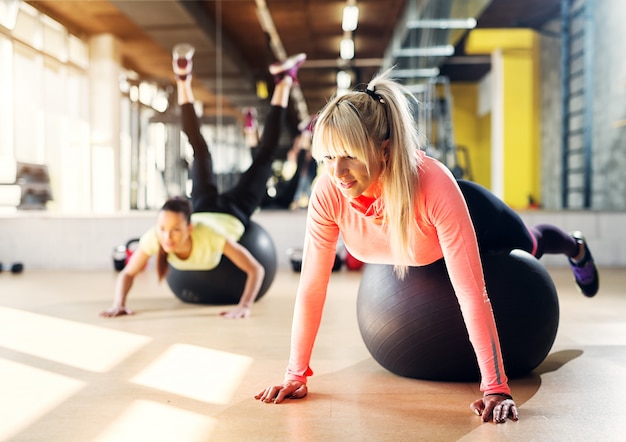 Deux jeunes filles concentrées dans un gymnase à l'aide de balles de pilates pour s'étirer après l'entraînement.