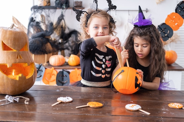 Deux jeunes filles diverses en costume de sorcière, s'amusant à la maison dans la cuisine, célébrant Halloween.