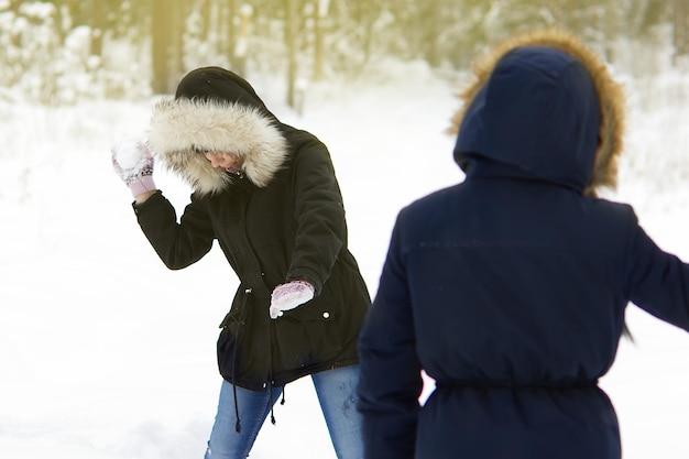 Deux jeunes filles jouent aux boules de neige sur fond de forêt d'hiver et de congères