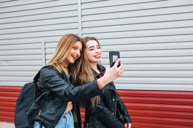 Deux jeunes filles prenant selfie à l'aide de smartphone en ville