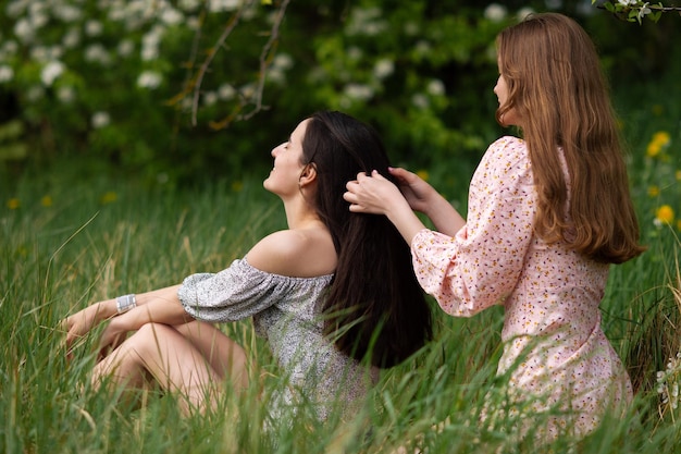 Deux jeunes filles en robes sont assises sous un arbre blanc et se tressent les cheveux