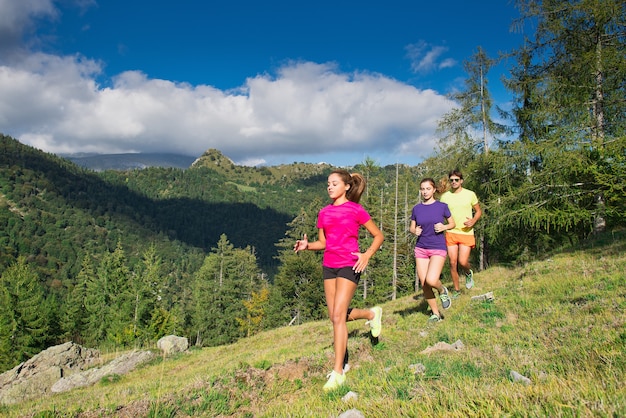 Deux jeunes filles sportives et un garçon courant ensemble sur l'herbe dans un paysage de montagne - Jogging dans la nature.