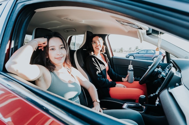 Deux jeunes filles en tenue sportive assises à l'intérieur de la voiture arrivant à la salle de sport ensemble pendant la journée avec une lumière parasite. Entraînement dur, concept d'attitude de remise en forme. Heureux de travailler ensemble