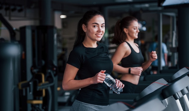 Deux jeunes filles en vêtements de sport sont ensemble dans la salle de sport au tapis roulant.