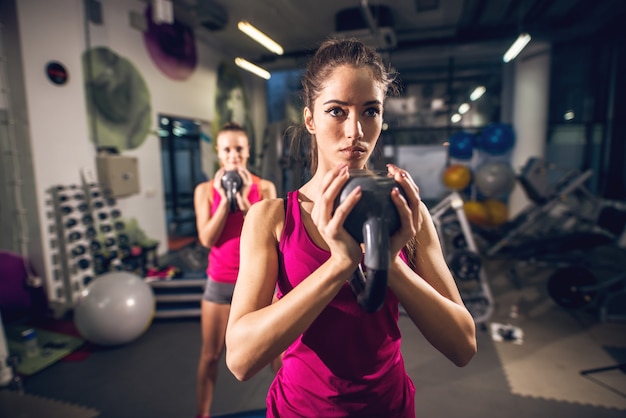 Deux jeunes forme athlétique mignon attrayant mince fitness filles actives faisant des exercices avec des kettlebells