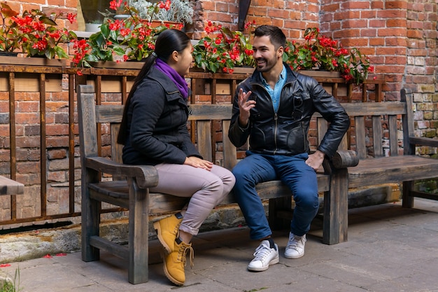 Deux jeunes un gars et une fille parlant assis sur un banc à l'extérieur