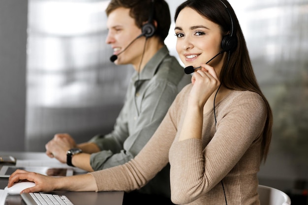 Photo deux jeunes gens en casque parlent aux clients, assis au bureau d'un bureau. concentrez-vous sur la femme. les opérateurs du centre d'appels au travail.