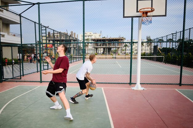 Deux jeunes hommes adultes jouent au basket-ball en plein air.