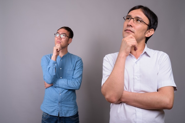 Deux jeunes hommes d'affaires asiatiques portant des lunettes ensemble contre un mur gris