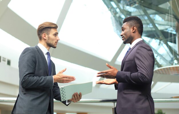 Deux jeunes hommes d'affaires multinationaux discutant des affaires lors d'une réunion au bureau.