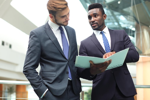 Deux jeunes hommes d'affaires multinationaux discutant des affaires lors d'une réunion au bureau.