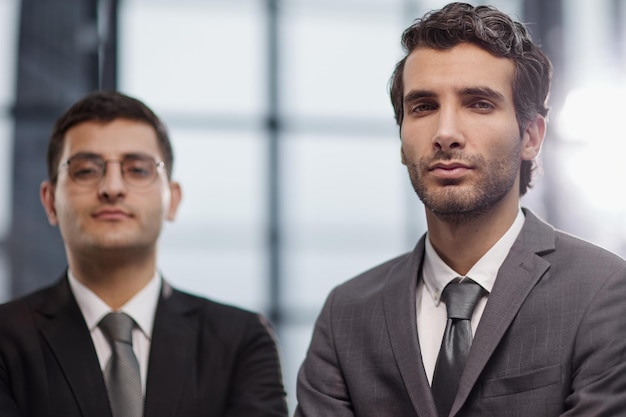 Deux jeunes hommes d'affaires sérieux debout avec les bras croisés au bureau