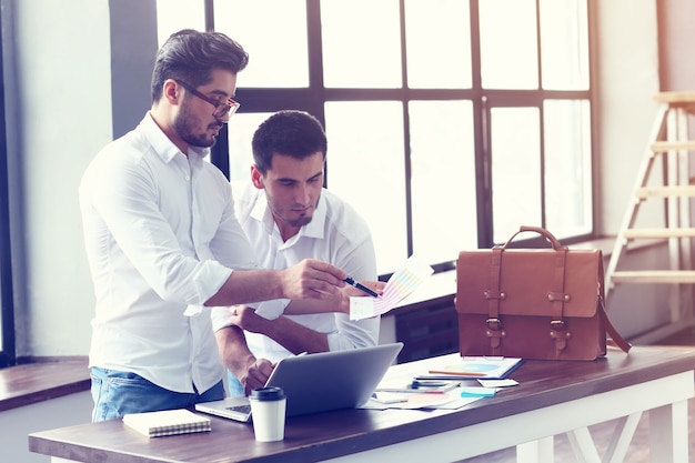 Deux jeunes hommes d'affaires travaillant sur un ordinateur portable au bureau moderne.Effet de film, lens flare