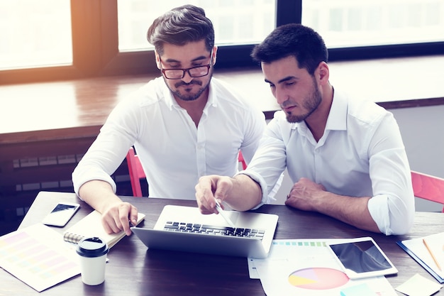 Deux jeunes hommes d'affaires travaillant sur un ordinateur portable au bureau moderne.Effet de film, lens flare