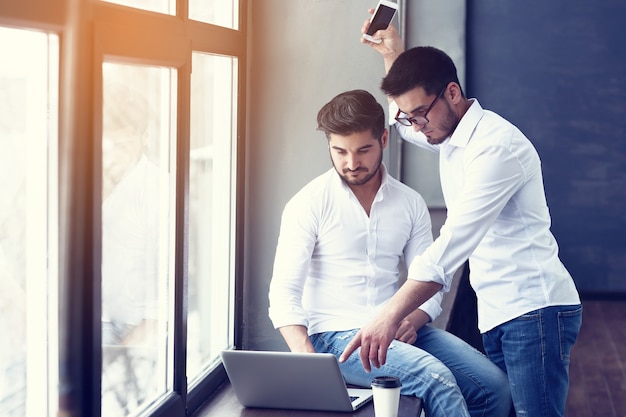 Deux jeunes hommes d'affaires travaillant sur un ordinateur portable au bureau moderne.Effet de film, lens flare