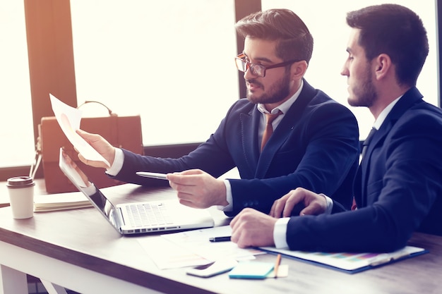 Deux jeunes hommes d'affaires travaillant sur ordinateur portable au bureau moderne. Hommes d'affaires hipster barbe. Effet de film, lens flare