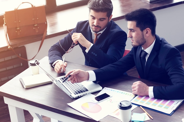 Deux jeunes hommes d'affaires travaillant sur ordinateur portable au bureau moderne. Hommes d'affaires hipster barbe. Effet de film, lens flare